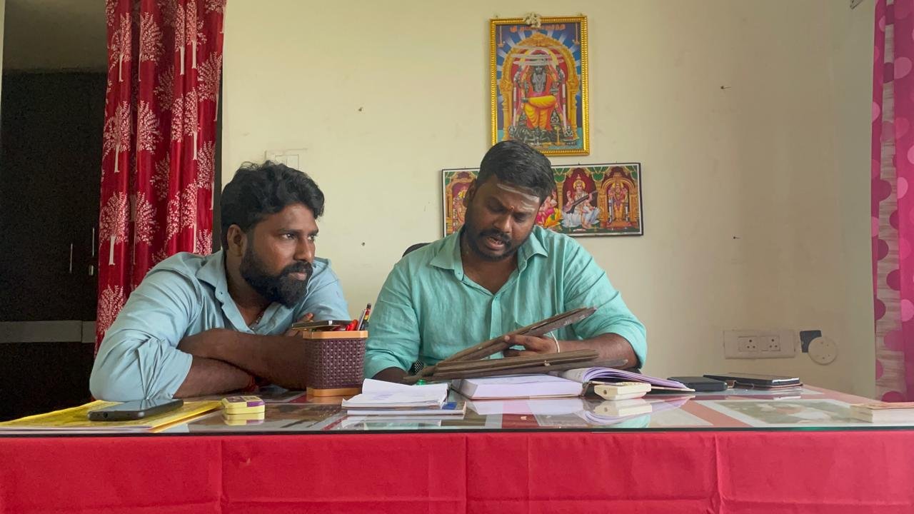 Guruji reviewing a palm-leaf manuscript with a seeker at the desk